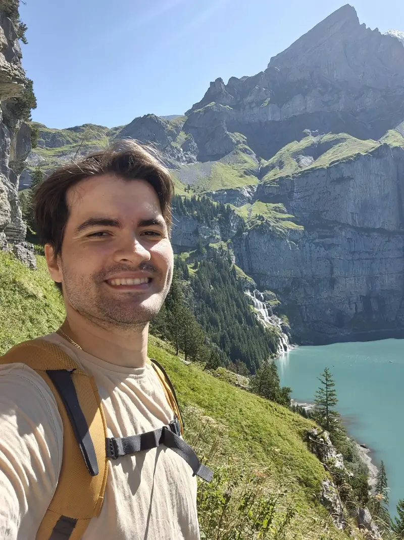 Portrait of Tomasz Opałka smiling in the Swiss mountains, a turquoise lake behind him